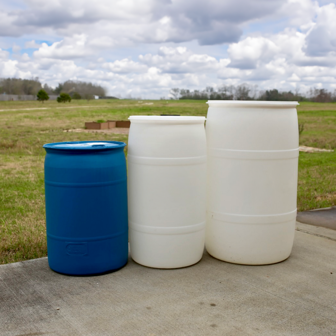 Three little rain barrels standing all in a row against a cloudy sky. One is blue, the other two are white.